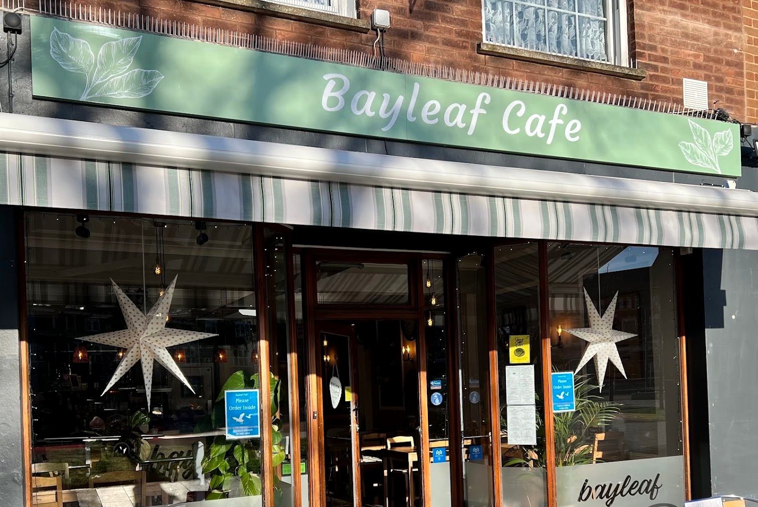 The Bayleaf Cafe shopfront: a sage-green sign with the name in white script and leaf drawings, a striped awning and tall windows hung with paper stars