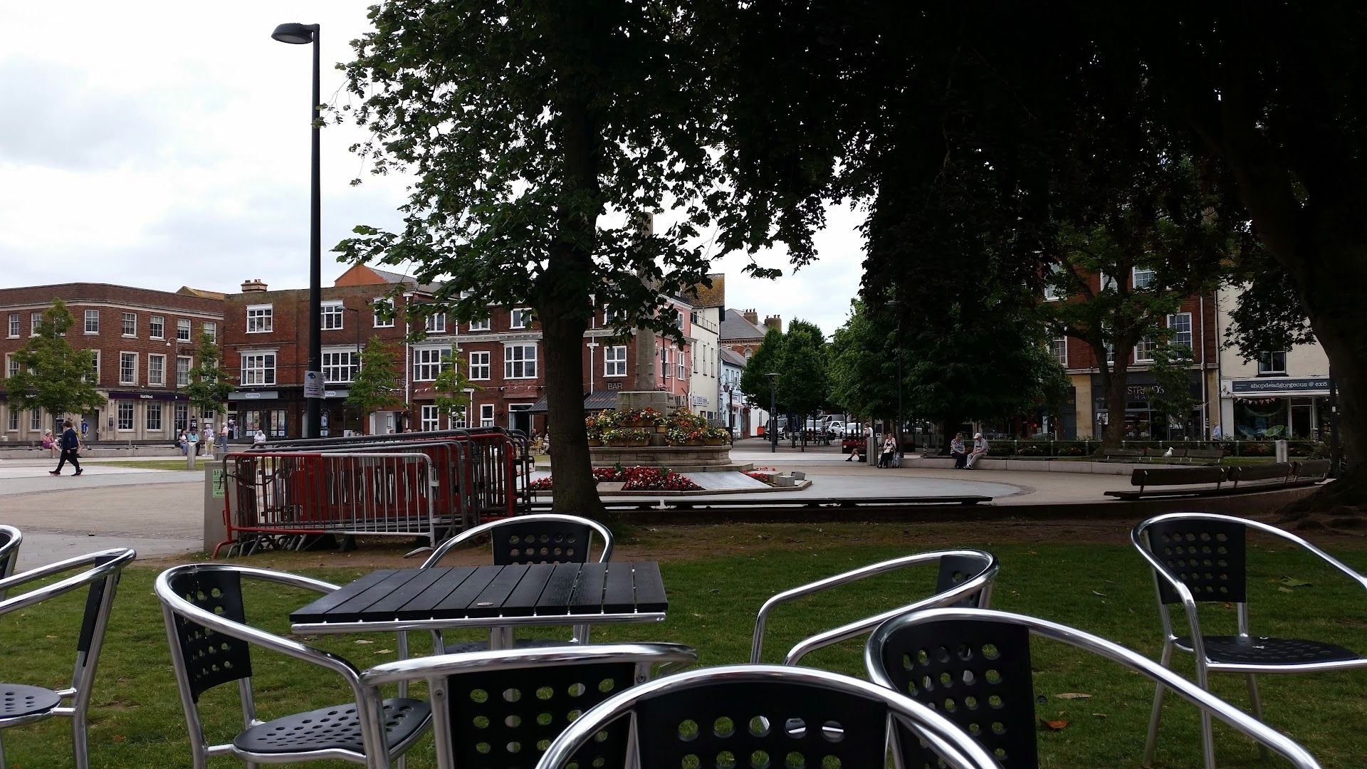 Metal café chairs and tables outside, looking across to the trees and flower beds of the Strand gardens